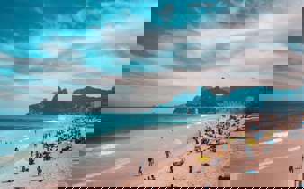 View of Ipanema Beach with beachgoers, ocean waves, and the Two Brothers Mountain in Rio de Janeiro, Brazil. 