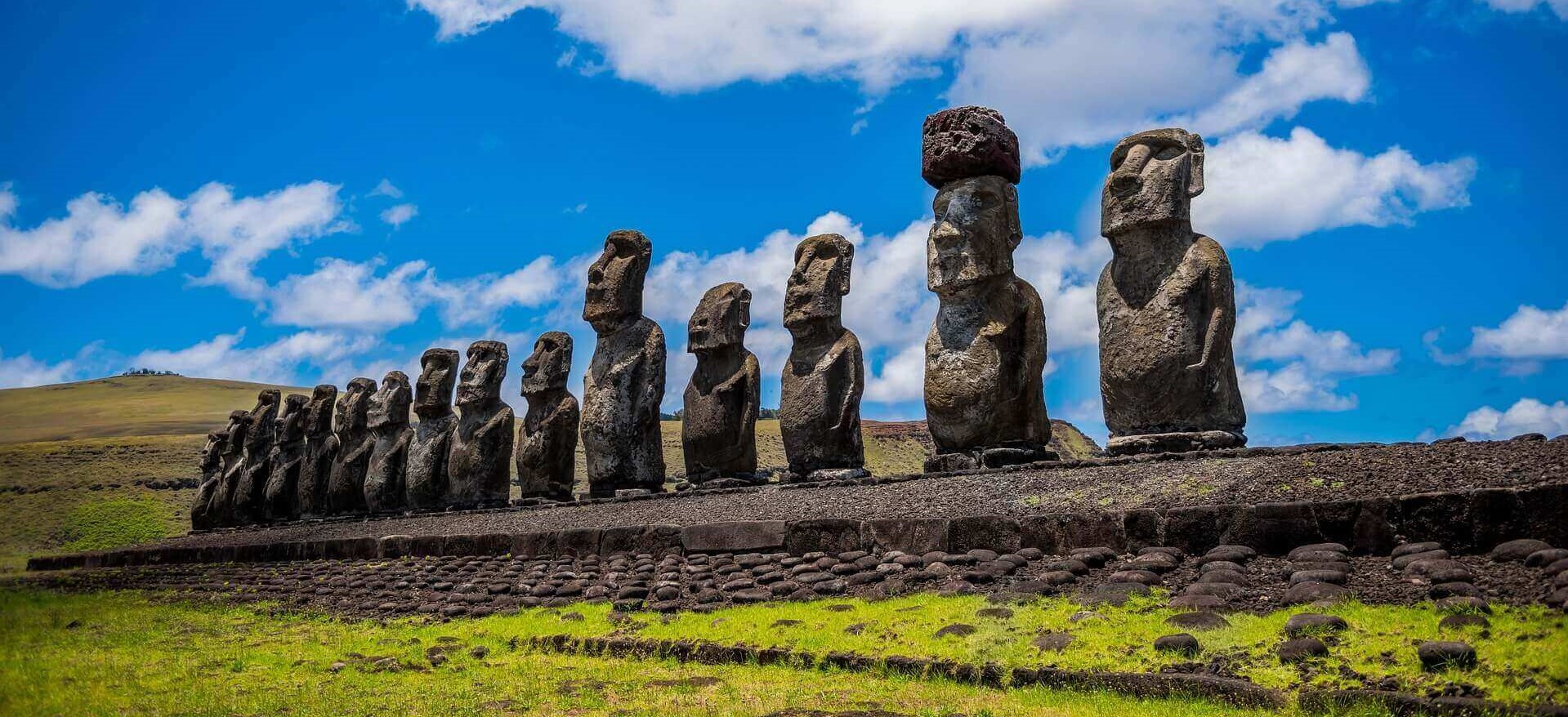 A row of towering Moai statues stands on a stone platform under a bright sky on Chile's Easter Island. 