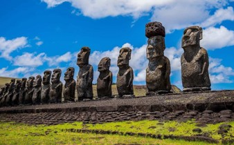 A row of towering Moai statues stands on a stone platform under a bright sky on Chile's Easter Island. 