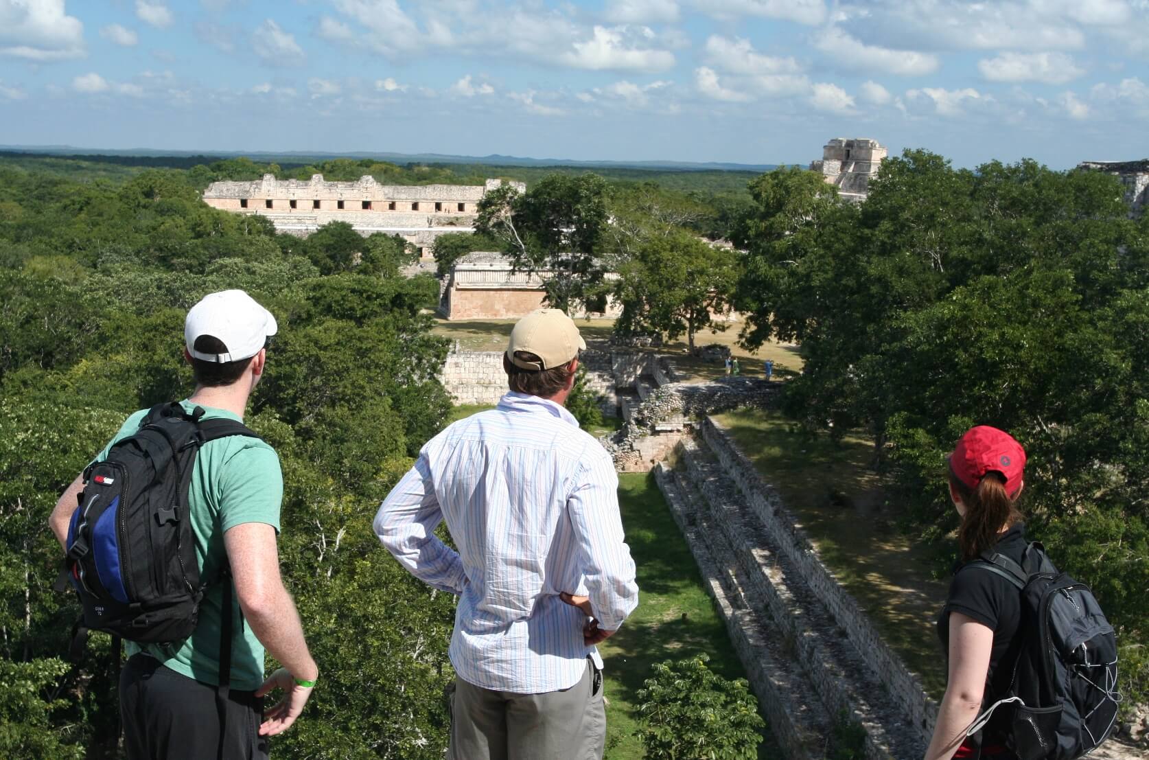 Tourists enjoying a panoramic view of the ancient Mayan ruins at Uxmal, Yucatan, Mexico, surrounded by dense green jungle. 