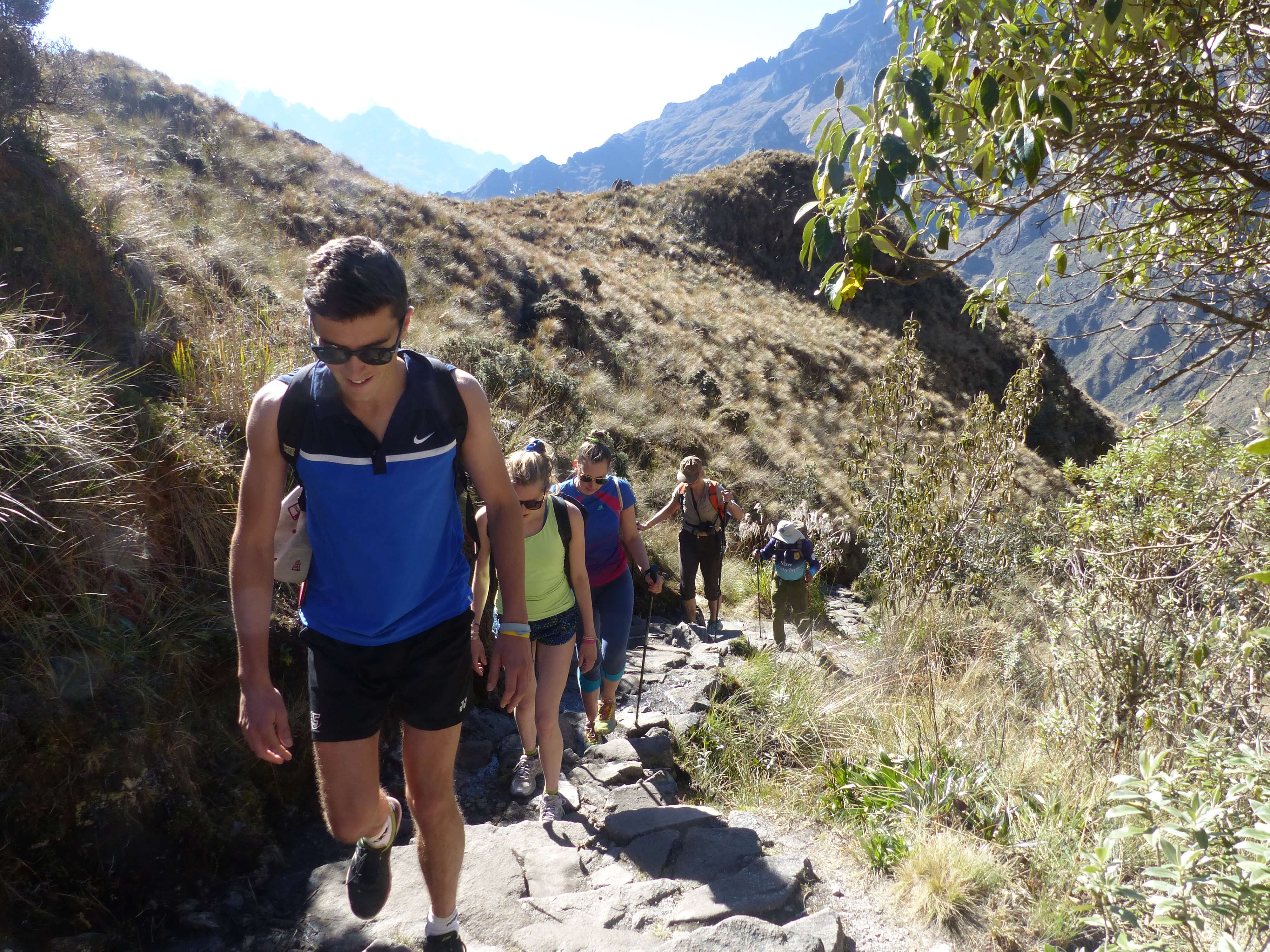 A family hikes together along a rugged mountain trail, immersed in Peru's Sacred Valley landscape. 