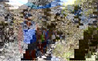 A family hikes together along a rugged mountain trail, immersed in Peru's Sacred Valley landscape. 