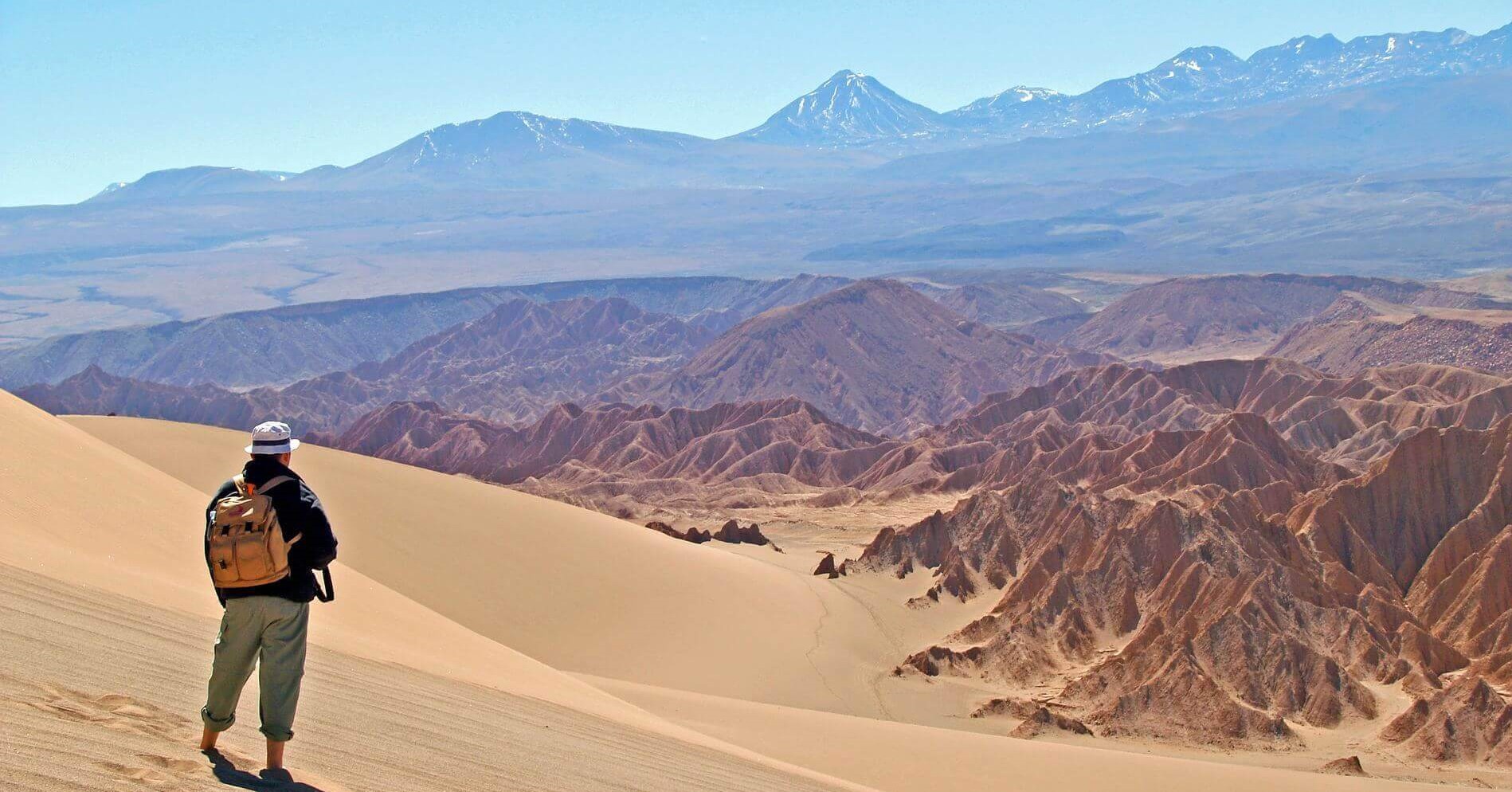 Hiker explores the vast, sunlit dunes of Chile's Atacama Desert with Andes backdrop. 