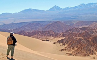 Hiker explores the vast, sunlit dunes of Chile's Atacama Desert with Andes backdrop. 