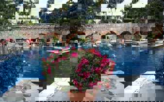 Charming Mexican hacienda with a serene pool, stone arches, and vibrant flowers in a tranquil garden setting. 