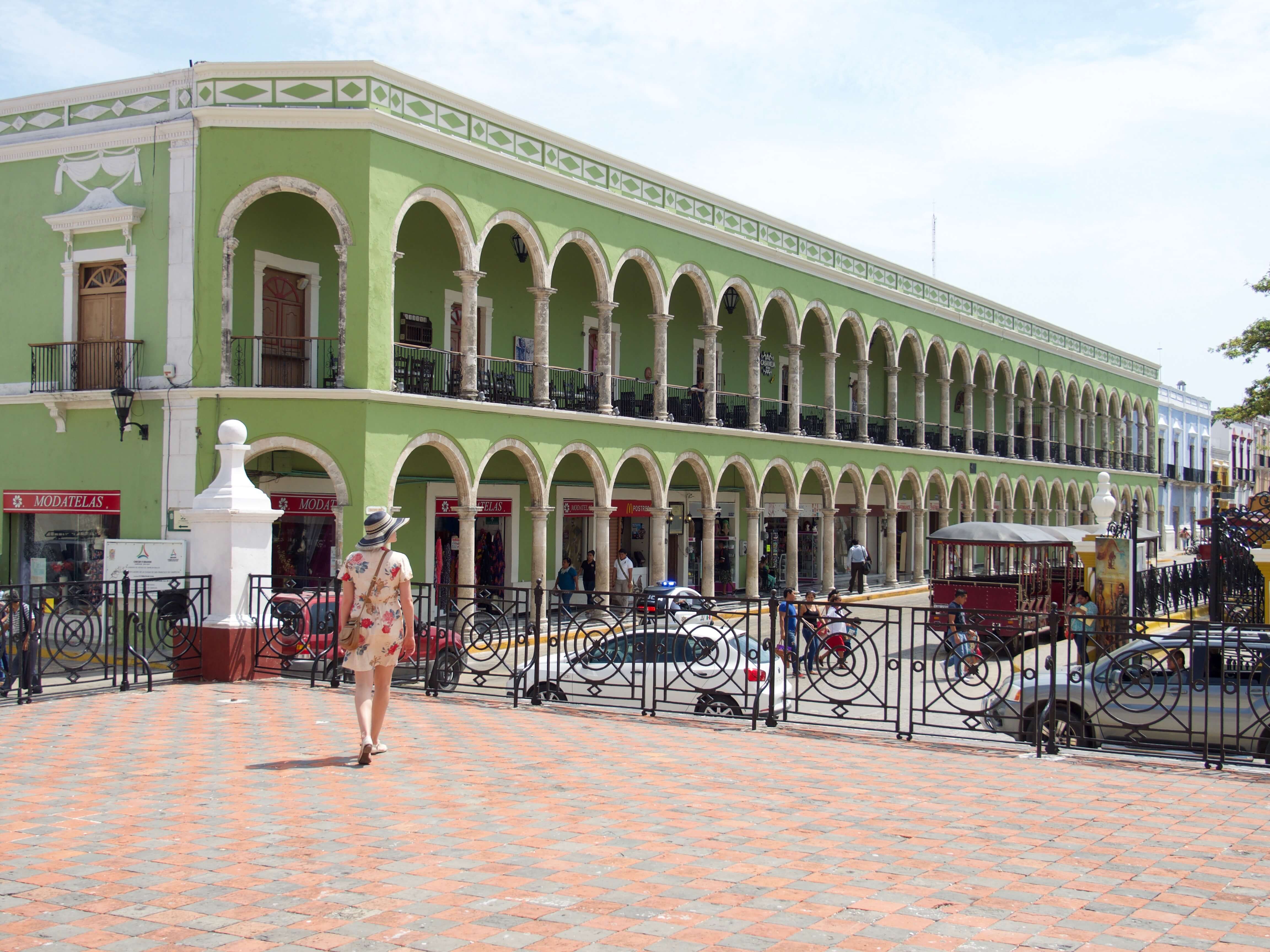 Historic green arcade building on Merida's Plaza Grande, Yucatan, with colonial arches, statue, and pedestrian view. 