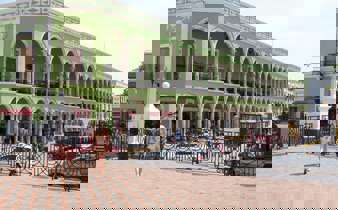 Historic green arcade building on Merida's Plaza Grande, Yucatan, with colonial arches, statue, and pedestrian view. 