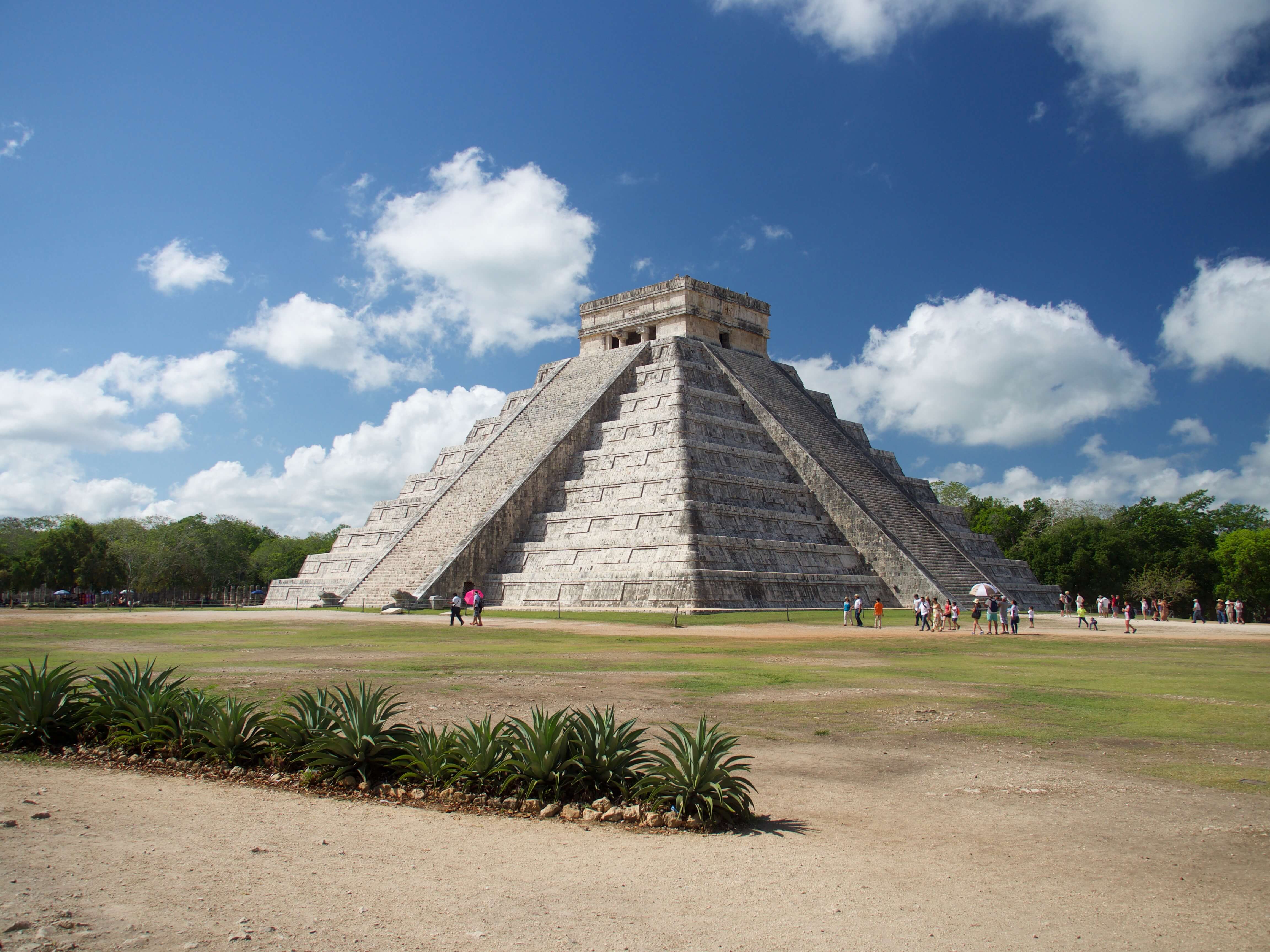 The Temple of Kukulcan at Chichen Itza rises under a bright sky, showcasing ancient Mayan architectural brilliance. 