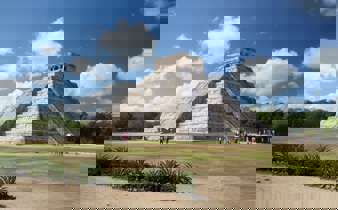 The Temple of Kukulcan at Chichen Itza rises under a bright sky, showcasing ancient Mayan architectural brilliance. 