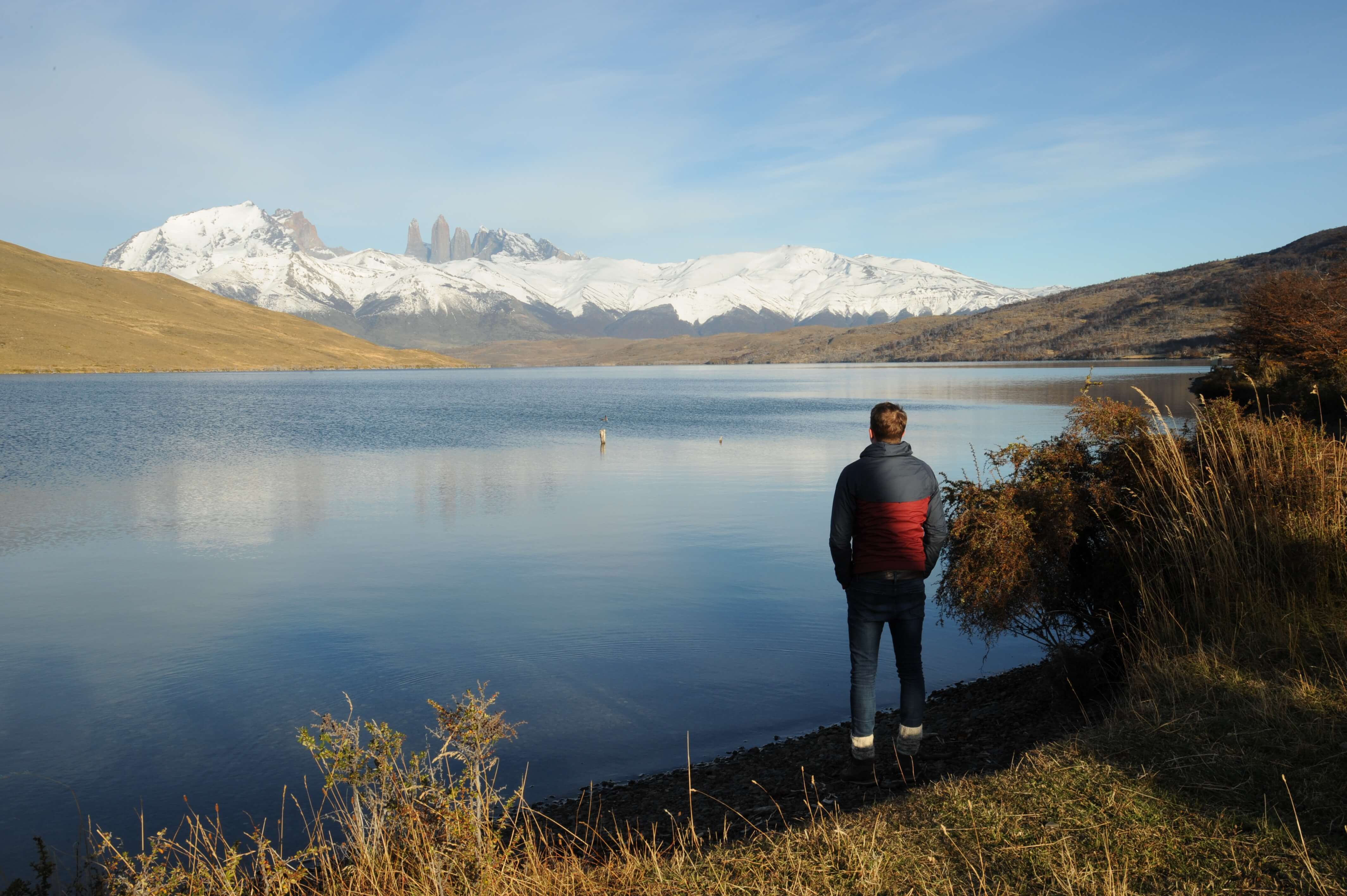 Traveler admires the reflection of the Paine Massif in a still Patagonia lake under clear skies in Torres del Paine, Chile. 