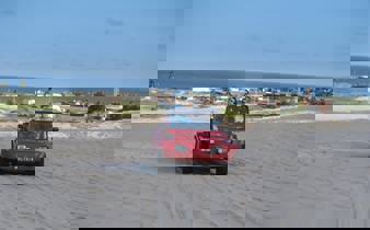 Red beach buggy driving  across sand dunes in Jericoacoara with ocean and coastal town in the background. 